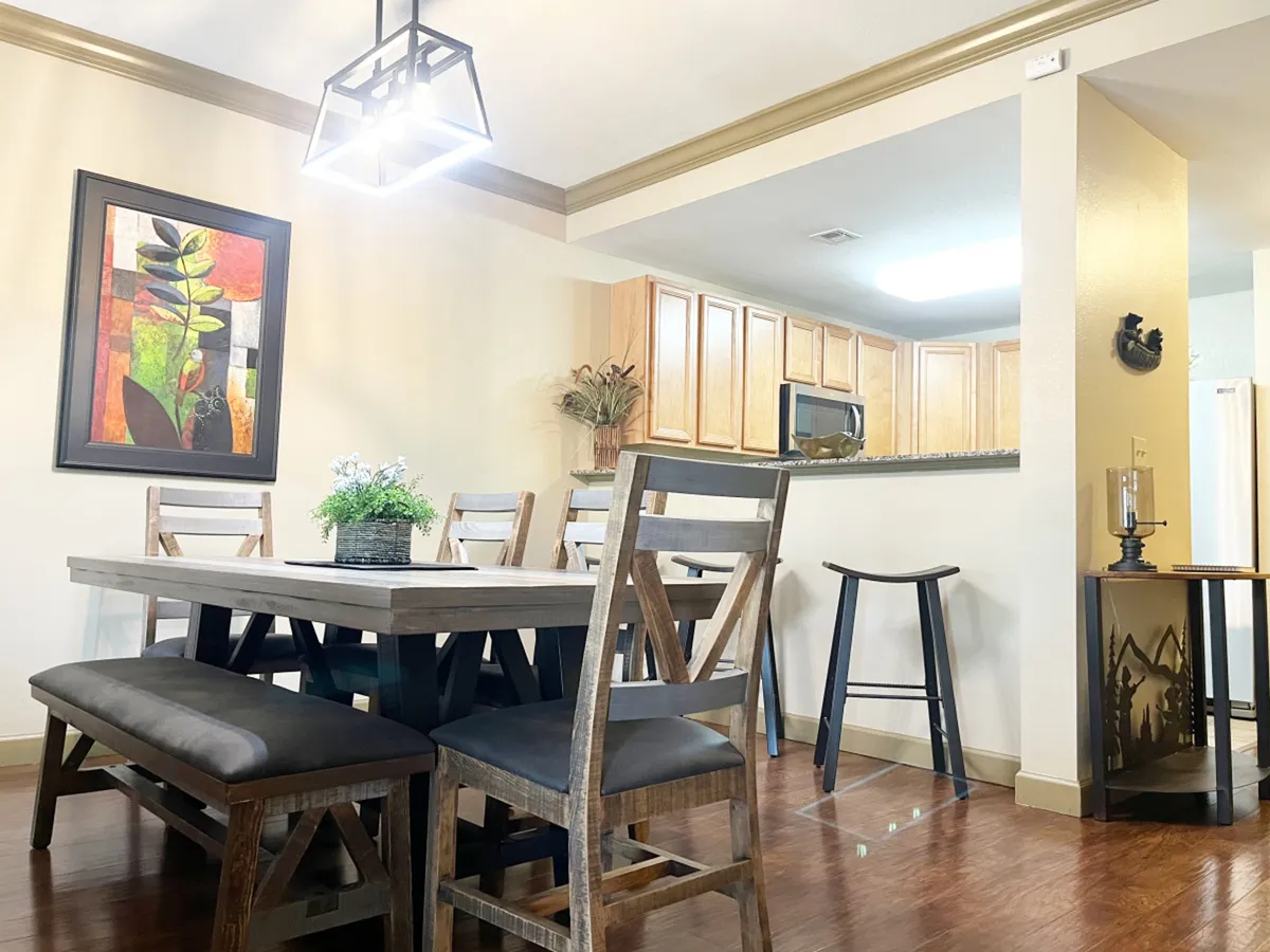 A cozy dining area set adjacent to the kitchen, featuring a family-sized dining table, decorative painting, and a view of the kitchen area. The space feels warm and inviting, designed for shared meals and memorable gatherings.