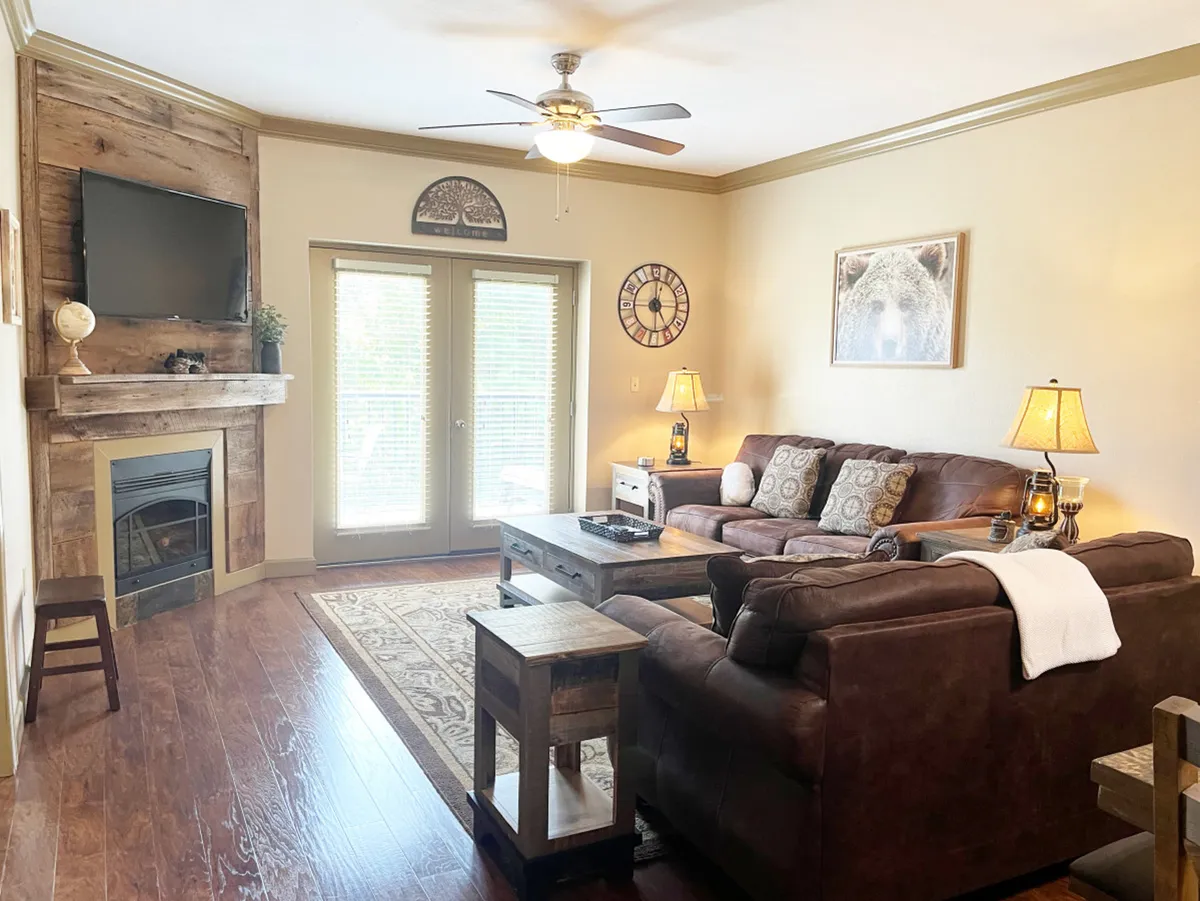 This image features a leather sofa positioned in front of a fireplace, accompanied by a coffee table and double doors leading directly outside. The scene is set for relaxing and socializing, with natural light streaming in through the doors, suggesting easy indoor-outdoor flow.