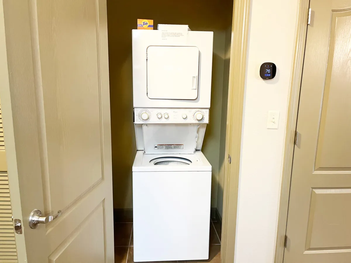 A practical nook with a stacked washer and dryer set, digital thermostat, and a nearby doorway, offering easy access and convenience for guests during their stay.