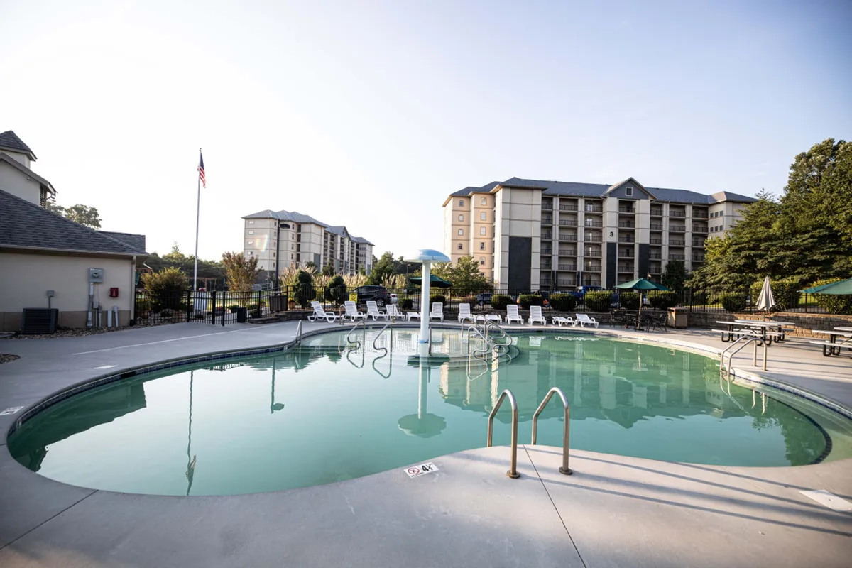 A sparkling swimming pool surrounded by lounge chairs and a decorative fountain, bordered by lush greenery. The environment feels lively yet relaxed, ideal for families looking to unwind or play together outdoors.